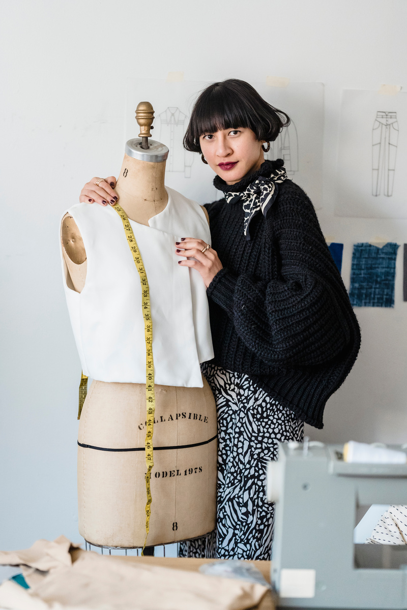 Stylish young ethnic fashion designer measuring mannequin in workshop